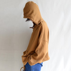 May include: A brown hooded sweatshirt with a drawstring closure. The sweatshirt has a relaxed fit and long sleeves.