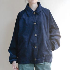 Puede incluir: Chaqueta de pana azul marino con cierre de botones, cuello y dos bolsillos delanteros. La chaqueta tiene mangas largas y está hecha de tela acanalada. Los botones son de color marrón claro.