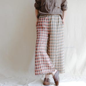 Puede incluir: Pantalones anchos a cuadros en rojo, blanco y beige. Los pantalones tienen un detalle de botón en el lateral y una cintura con cordón. La persona de la imagen lleva una camisa marrón con botones y zapatos marrones. Los pantalones son de estilo casual.