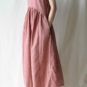 May include: A red and white gingham sleeveless dress with a gathered skirt and pockets. The dress is midi length and is worn with brown platform sandals.