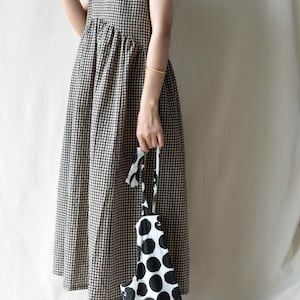 May include: A sleeveless black and white gingham dress with a gathered skirt. The dress is paired with a black and white polka dot tote bag.