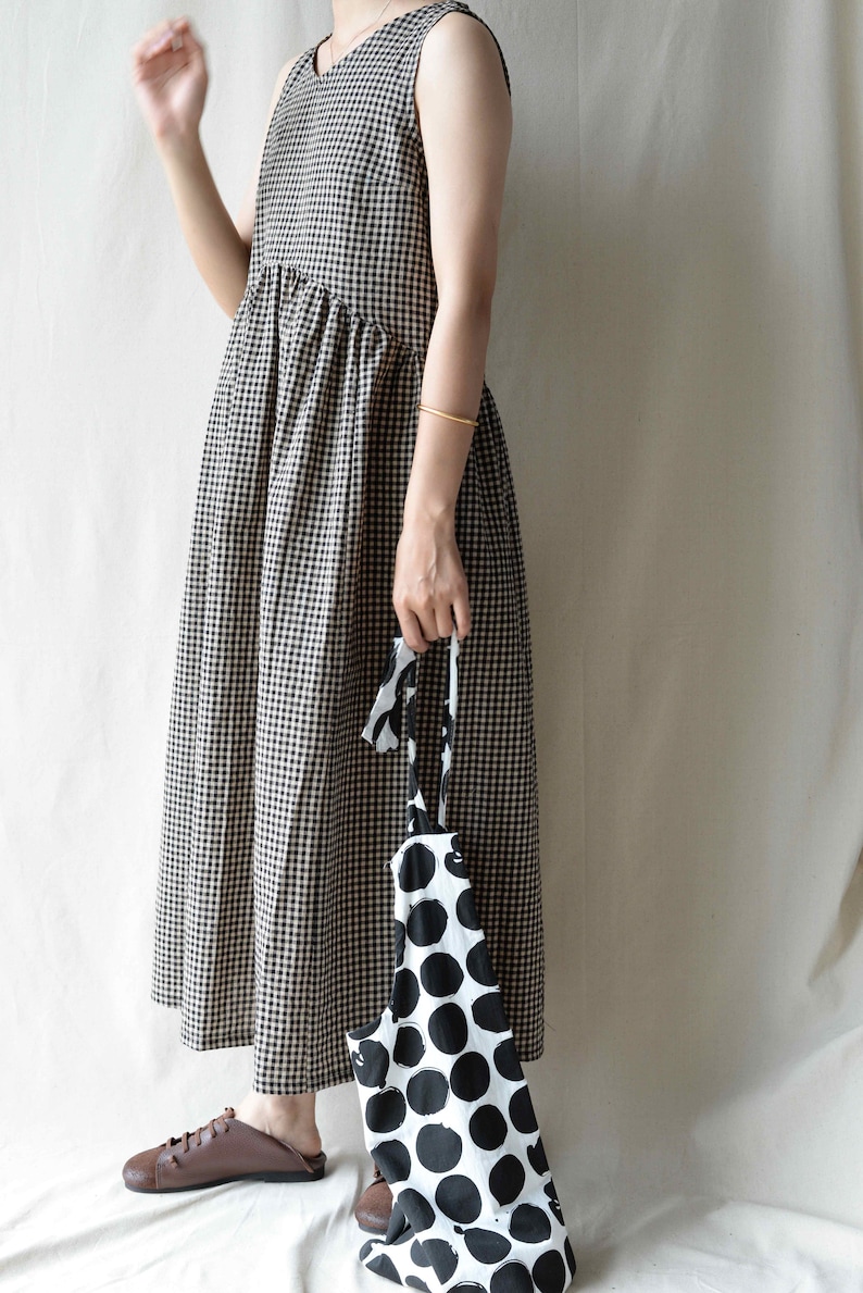 May include: A sleeveless black and white gingham dress with a gathered skirt. The dress is paired with a black and white polka dot tote bag.