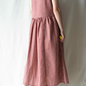 May include: A red and white gingham sleeveless dress with a gathered waistline. The dress is midi length and has a relaxed fit.