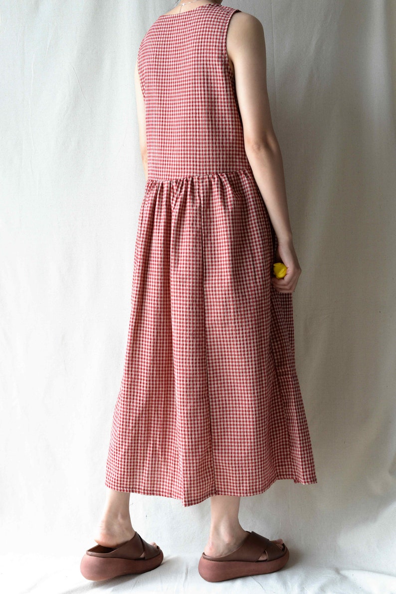 May include: A red and white gingham sleeveless dress with a gathered waistline. The dress is midi length and has a relaxed fit.