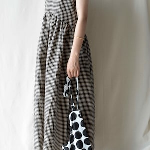 May include: A sleeveless black and white gingham dress with a gathered waist. The dress is paired with brown leather shoes and a black and white polka dot tote bag.