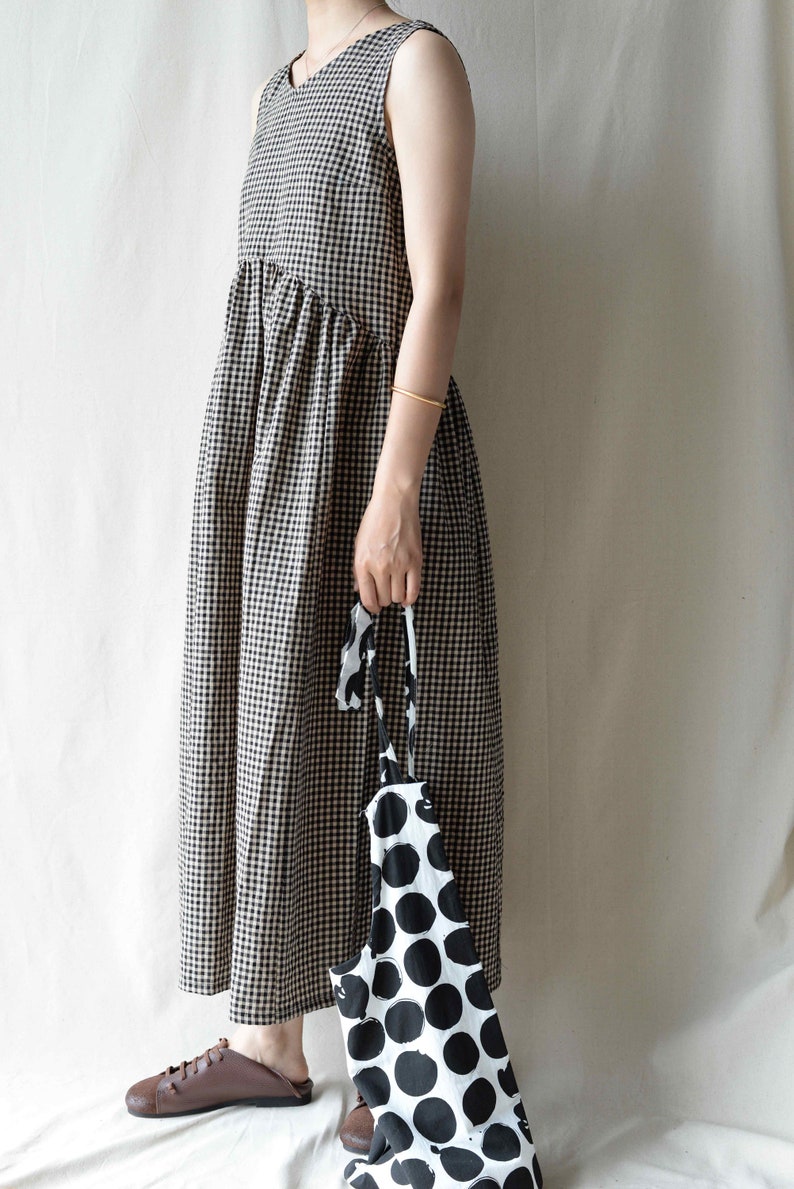 May include: A sleeveless black and white gingham dress with a gathered waist. The dress is paired with brown leather shoes and a black and white polka dot tote bag.