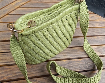 Könnte beinhalten: Eine grüne geflochtene Strohtasche mit einem goldenen Metallverschluss und einem langen Schulterriemen. Die Tasche hat ein Chevron-Muster.