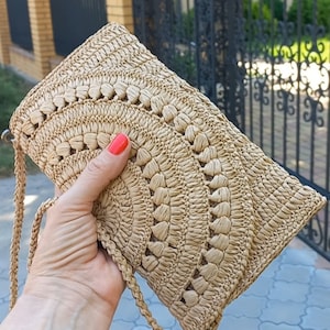 Puede incluir: Un bolso de mano de paja tejido con una correa marr&oacute;n. El bolso tiene un dise&ntilde;o de crochet con un patr&oacute;n circular.