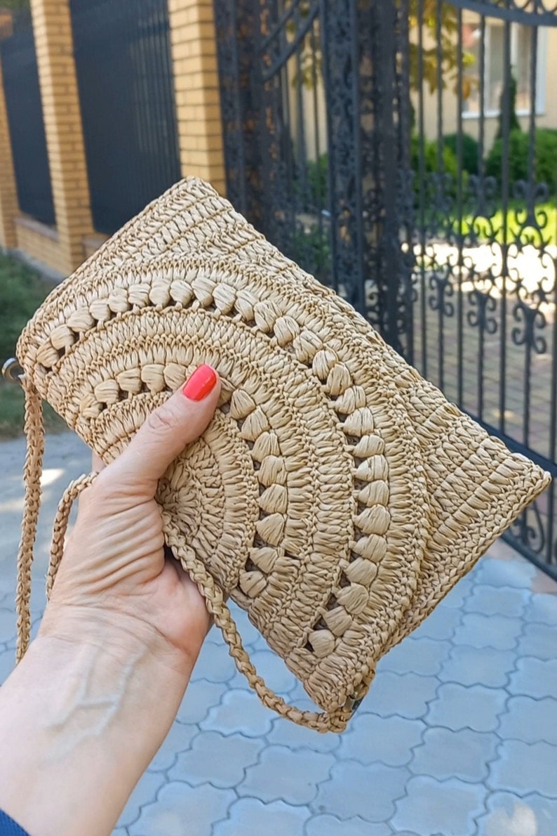 Puede incluir: Un bolso de mano de paja tejido con una correa marr&oacute;n. El bolso tiene un dise&ntilde;o de crochet con un patr&oacute;n circular.