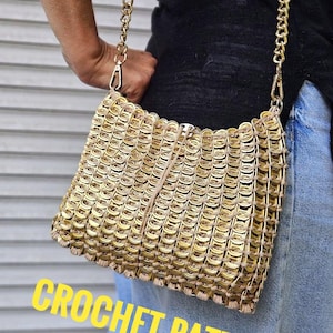 Pode incluir: Uma bolsa de crochê dourada com alça de corrente. A bolsa é feita de peças de metal interligadas, com o texto "CROCHET PATTERN" em amarelo na parte inferior. A bolsa é retangular com fecho de zíper.