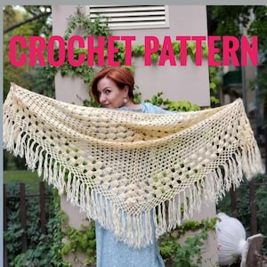 Könnte beinhalten: Ein gehäkeltes Tuch mit einem zarten Muster und Fransen. Das Tuch ist hellcremefarben und liegt über den Schultern einer Person.