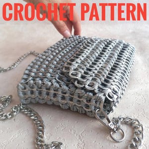 May include: A handmade silver crochet bag with a chain strap. The bag is made from recycled materials, possibly pull tabs, and features a rectangular shape with a flap closure. The words "CROCHET PATTERN" are in red text at the top.