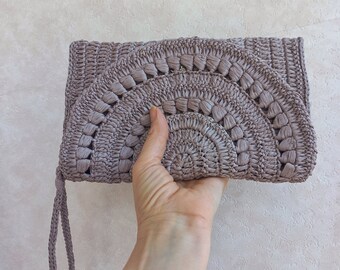 May include: A light gray crocheted clutch bag with a circular design. The bag has a long strap.