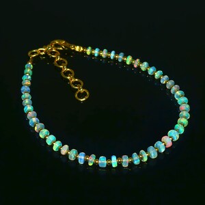 May include: A delicate gold chain bracelet with a row of iridescent opal beads. The beads are a gradient of colors, ranging from light blue to pink.