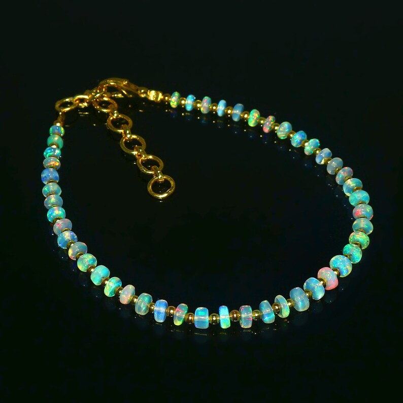 May include: A delicate gold chain bracelet with a row of iridescent opal beads. The beads are a gradient of colors, ranging from light blue to pink.