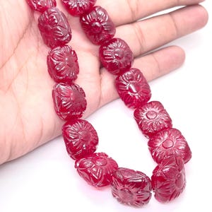 May include: A strand of carved ruby beads. Each bead is a deep red colour and features a floral design. The beads are rectangular with rounded edges and are strung together, creating a necklace or bracelet.