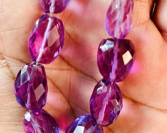 May include: A strand of faceted amethyst beads in shades of purple and lavender. The beads are oval shaped and have a smooth, polished finish.