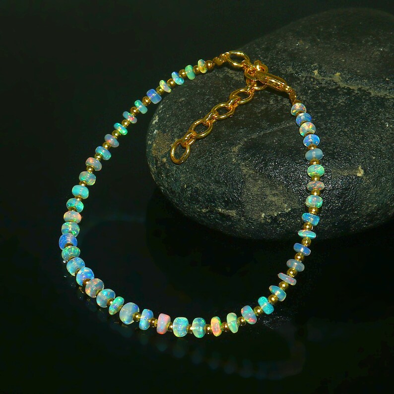 May include: A delicate gold bracelet with a chain clasp, featuring a row of iridescent opal beads.