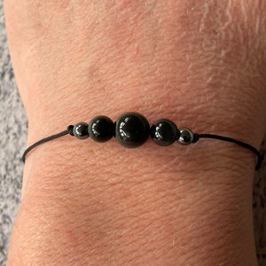 May include: A black string bracelet with four black beads and two silver beads.