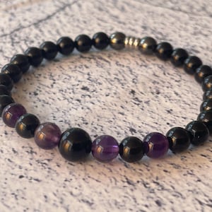 May include: Black and purple beaded bracelet with a silver clasp. The bracelet is made with black onyx and amethyst beads.
