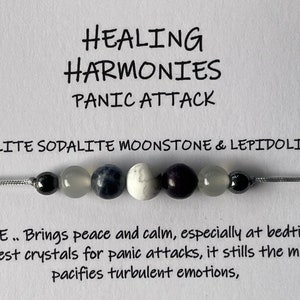 May include: A bracelet made with howlite, sodalite, moonstone, and lepidolite beads. The bracelet is designed to help with panic attacks. The text on the card reads "HEALING HARMONIES PANIC ATTACK HOWLITE SODALITE MOONSTONE & LEPIDOLITE HOWLITE.. Brings peace and calm, especially at bedtime. One of the best crystals for panic attacks, it stills the mind and pacifies turbulent emotions."