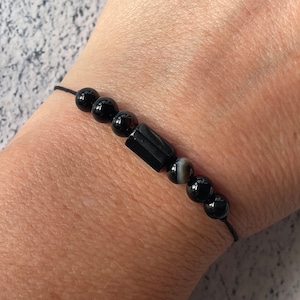 May include: A black beaded bracelet with a black and white agate bead and a black rectangular bead.