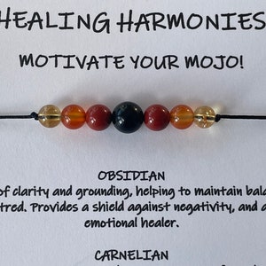 Puede incluir: Un brazalete de cuerda negra con cuentas marrones, naranjas y negras. El brazalete está etiquetado como "Healing Harmonies" y "Motivate Your Mojo!" El texto "Obsidian" está debajo del brazalete y describe la cuenta negra como una piedra de claridad y conexión a tierra. El texto "Carnelian" está debajo de la descripción de la cuenta de obsidiana.