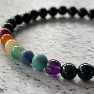 May include: A black beaded bracelet with seven colourful gemstone beads. The beads are red, orange, yellow, green, blue, turquoise, and purple.