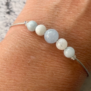 May include: A silver bracelet with light blue and white beads. The bracelet is on a person's wrist.