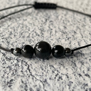 May include: A black beaded bracelet with a black cord and silver beads. The bracelet is adjustable.