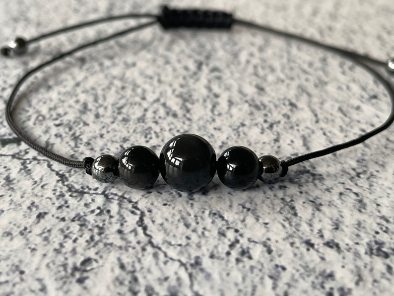 May include: A black beaded bracelet with a black cord and silver beads. The bracelet is adjustable.
