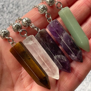 May include: Five crystal point pendants on silver chains with silver bead accents. The pendants are in the colors of clear, green, brown, purple, and amethyst.