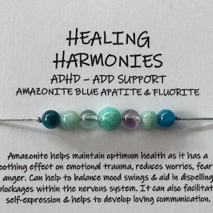 May include: A white card with the text "HEALING HARMONIES ADHD-ADD SUPPORT AMAZONITE BLUE APATITE & FLUORITE" and a string of green and blue beads.