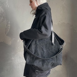 May include: A large, slouchy black shoulder bag with a textured, distressed finish. The bag features two long black straps, silver-toned metal hardware, and a wide, adjustable crossbody strap attached with metal clips on the sides.