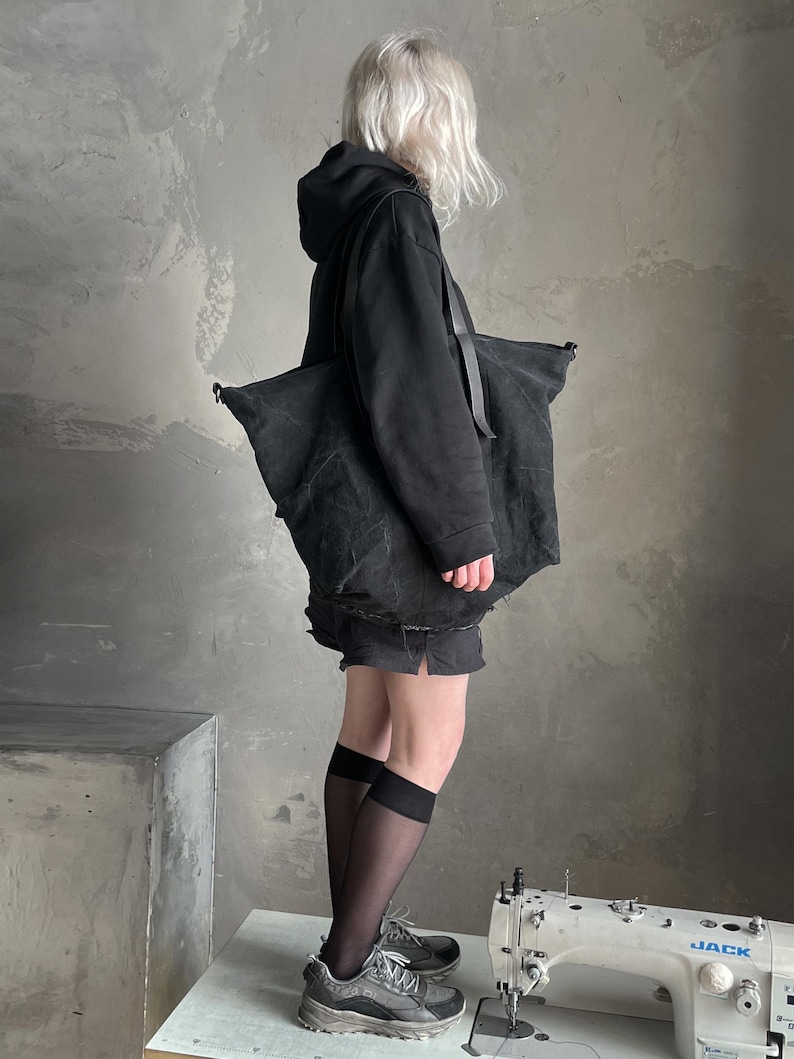 May include: A large black canvas tote bag with a textured finish and black shoulder straps. The bag features a spacious main compartment and is carried over the shoulder. The material appears durable and matte, providing a functional accessory for daily use.
