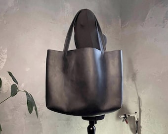 Könnte beinhalten: Eine schwarze Ledertasche mit einfachem Design. Die Tasche wird auf einem schwarzen Ständer präsentiert.