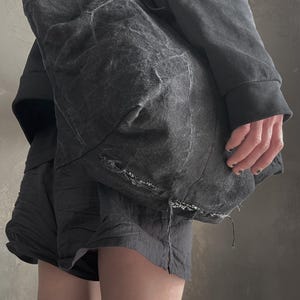 May include: A large, slouchy charcoal grey tote bag made of a textured, distressed fabric with visible frayed edges and a worn, washed-out appearance. The bag features a spacious, unstructured design with a deep, dark grey tone and subtle variations.