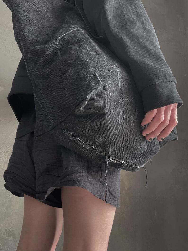 May include: A large, slouchy charcoal grey tote bag made of a textured, distressed fabric with visible frayed edges and a worn, washed-out appearance. The bag features a spacious, unstructured design with a deep, dark grey tone and subtle variations.