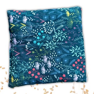 Pode incluir: Uma almofada de tecido azul-esverdeado com um padrão floral em tons de rosa, branco, azul e amarelo. A almofada é recheada com arroz e pode ser aquecida no microondas para uma terapia de calor reconfortante.