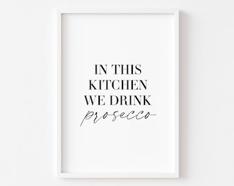 Op de afbeelding: Een wit ingelijst print met zwarte tekst die "In deze keuken drinken we prosecco" luidt.