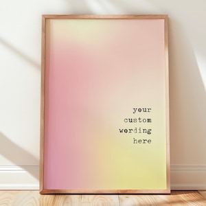 May include: A rectangular wall art print in a light wooden frame featuring a soft, blurred gradient background transitioning from pale pink to yellow. The text 'your custom wording here' is printed in a black, typewriter-style font on the right.