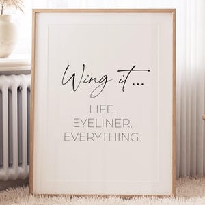 May include: A framed print with the text "Wing it... Life. Eyeliner. Everything." in black lettering on a white background.