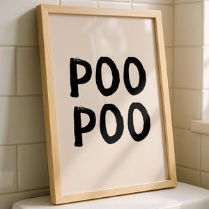 Può includere: Una stampa incorniciata con la parola "POO" ripetuta due volte in lettere nere in grassetto. La stampa ha uno sfondo beige chiaro e una cornice in legno naturale. La stampa è esposta sopra un water in un bagno.