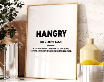 Könnte beinhalten: Ein goldfarbener gerahmter Druck mit dem Wort "HANGRY" in schwarzem Text. Die Definition von Hangry ist "ein Zustand der Wut, der durch einen Mangel an Nahrung verursacht wird und eine negative Veränderung des emotionalen Zustands bewirkt."