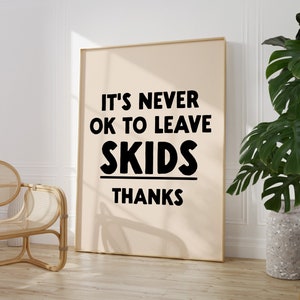 May include: A beige poster with black text that reads "It's never ok to leave skids thanks". The poster is framed in a light wood frame and is hanging on a white wall.