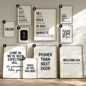 Op de afbeelding: Een verzameling ingelijste wandkunst met verschillende tekstgebaseerde ontwerpen. De kunstwerken bevatten zinnen als "OH.HI!", groeten in meerdere talen en humoristische uitspraken zoals "Please remove your shoes and your drama."