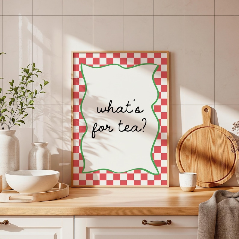 Peut inclure: Une affiche encadr&eacute;e avec le texte "what's for tea ?" dans une police fantaisiste. Le cadre a une bordure &agrave; carreaux rouges et blancs avec un bord int&eacute;rieur vert ondul&eacute;. L'affiche est expos&eacute;e sur un comptoir de cuisine.