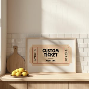 May include: A framed print featuring a custom ticket design. The ticket is tan with a red border and the words "CUSTOM TICKET" and "ADMIT ONE" in black. The print is displayed on a wooden surface with lemons and a cutting board.