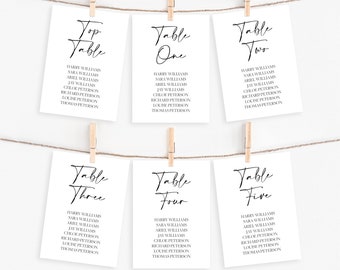 May include: Six white cards with black calligraphy text, clipped to a string with wooden clothespins. Each card lists names under the headings "Top Table," "Table One," "Table Two," "Table Three," "Table Four," and "Table Five."