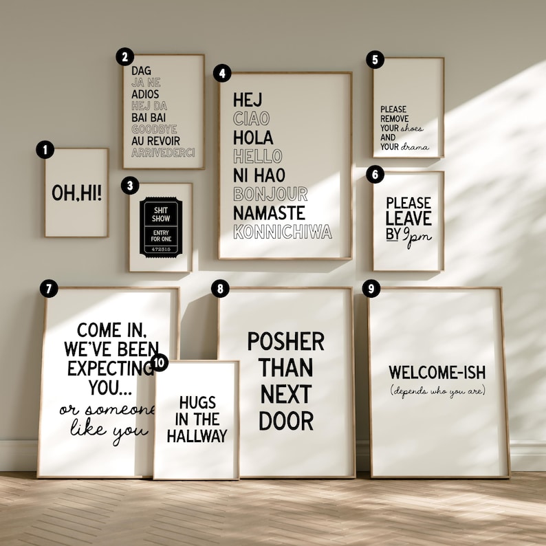 Op de afbeelding: Een verzameling ingelijste wandkunst met verschillende tekstgebaseerde ontwerpen. De kunstwerken bevatten zinnen als "OH.HI!", groeten in meerdere talen en humoristische uitspraken zoals "Please remove your shoes and your drama."